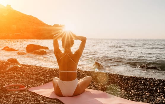 Young woman in swimsuit with long hair practicing stretching outdoors on yoga mat by the sea on a sunny day. Women's yoga fitness pilates routine. Healthy lifestyle, harmony and meditation concept.