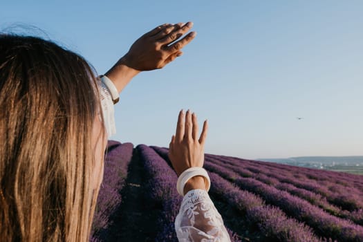 Close up portrait of young beautiful woman in a white dress and a hat is walking in the lavender field and smelling lavender bouquet.