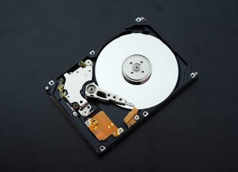 Disassembled open hard disk drive HDD of computer or laptop lies on dark matte surface. Сomputer hardware and equipment. Harddisk data storage.