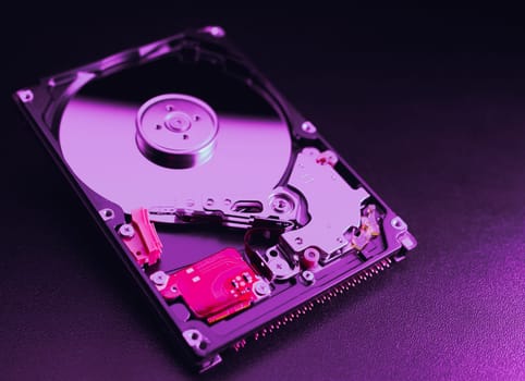 An open hard disk disassembled HDD of a computer or laptop lies on a purple surface. Computer hardware and accessories. Hard disk storage.