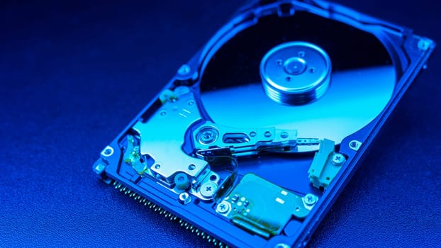 An open hard disk disassembled HDD of a computer or laptop lies on a blue surface. Computer hardware and accessories. Hard disk storage.