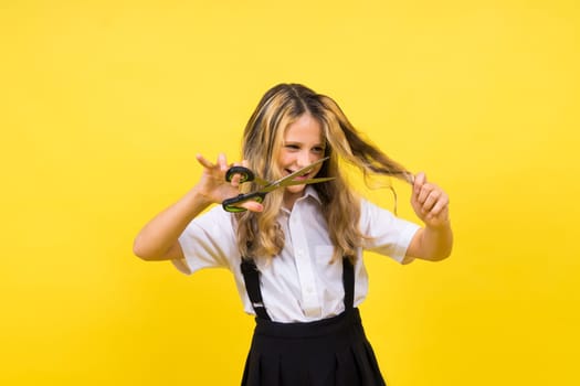 A young girl about to cut her own hair with pair of scissors, isolated against yellow background