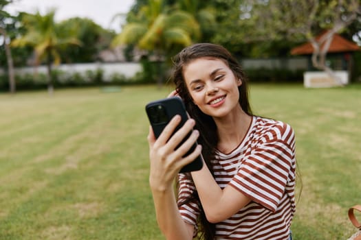 lifestyle woman tree cell smile green adult park browsing blogger spring outdoor cellphone phone human happy shirt beautiful palm grass smiling nature