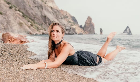 Woman travel sea. Young Happy woman in a long red dress posing on a beach near the sea on background of volcanic rocks, like in Iceland, sharing travel adventure journey