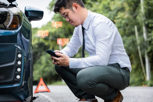 Businessman calling roadside assistance after his car broke down on the road. Waiting for help and support, he sits by his car wearing a white shirt. Concept of roadside assistance and car accident