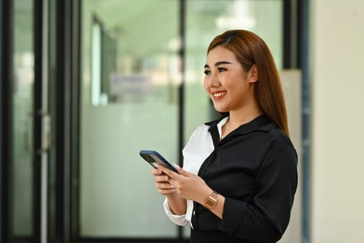 Attractive female investment advisor holding smartphones and looking out of the window, daydreaming, visualizing future.