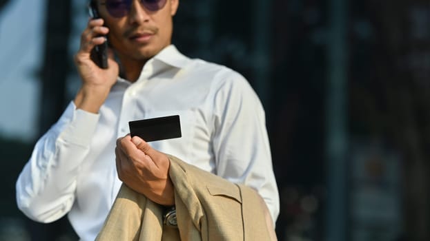 Worried millennial man holding credit card and talking on smartphone with customer service, having problem with credit card or payment.