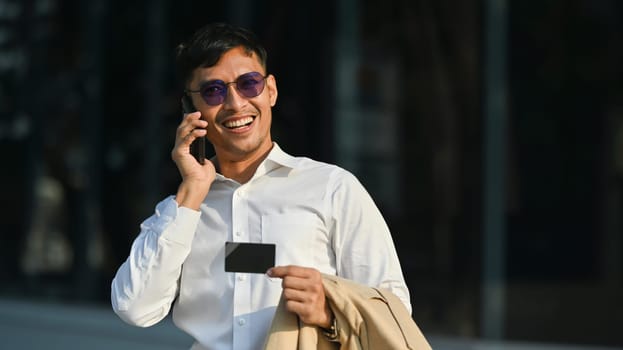 Smiling businessman talking on mobile phone with bank client support operator while walking in business district.
