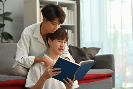 Peaceful two asian male lovers embracing each other and reading book in cozy living room. Homosexual and love concept.
