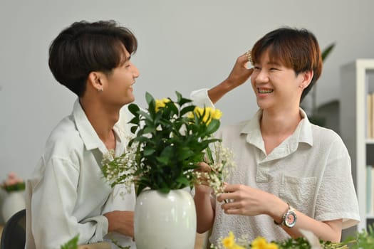 Happy male gay couple spending time together, creating beautiful bouquet with different flowers at home. LGBT, homosexual and love.