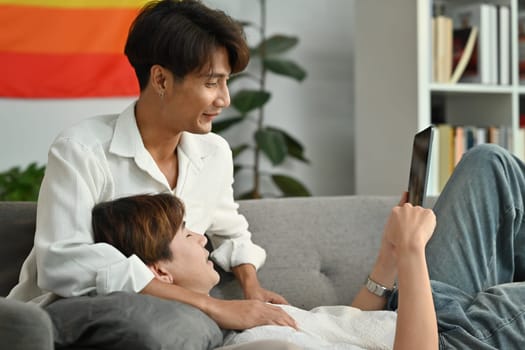 Carefree male gay couple using browsing internet on digital tablet and relaxing on couch. Love and lifestyle relationship concept.