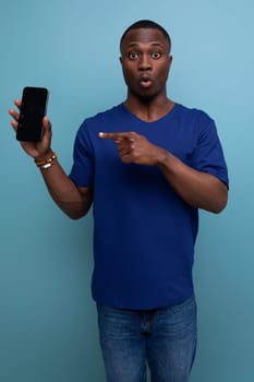 handsome young american man in blue t-shirt holding phone with screen mockup.