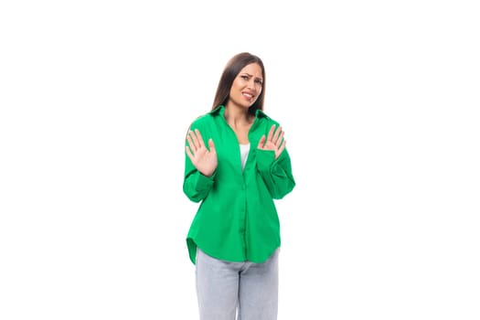 shy young caucasian brunette lady with make-up dressed in an elegant green shirt on a white background with copy space.