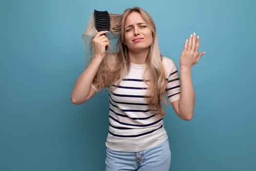 sullen upset blond woman with difficulty combing her hair on a blue background.