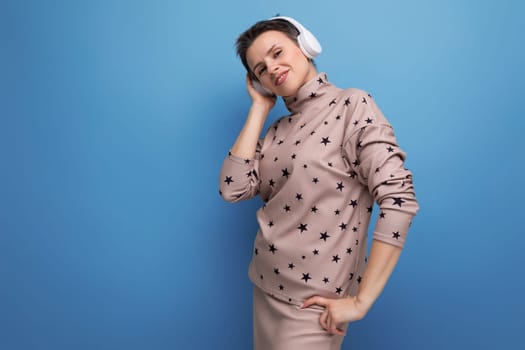active bright caucasian young woman with a short haircut dressed in a beige suit listens to music in wireless bluetooth headphones.