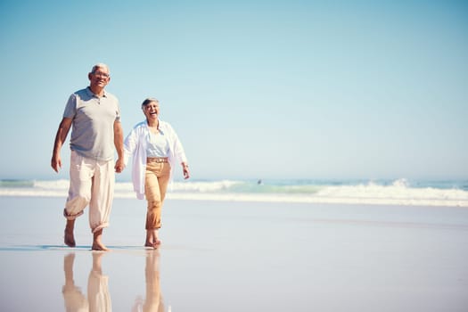 Holding hands, summer and an old couple walking on the beach with a blue sky mockup background. Love, romance or mock up with a senior man and woman taking a walk on the sand by the ocean or sea.