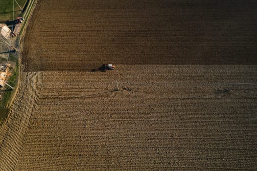 farmer driving a crawler tractor drags a cloud of dust behind, ploughing, power harrowing surface crust breaking to facilitate the birth and seeding of plants on dry soil