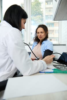 Adult pregnant woman at appointment with female doctor, obstetrician gynecologist. General practitioner taking blood pressure in office to early diagnostic and prevent pregnancy induced hypertension