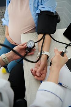 Early diagnostic, prevention and treatment of hypertension, pre-eclampsia and eclampsia in pregnancy. Close-up of obstetrician doctor, gynecological nurse measuring blood pressure of pregnant woman
