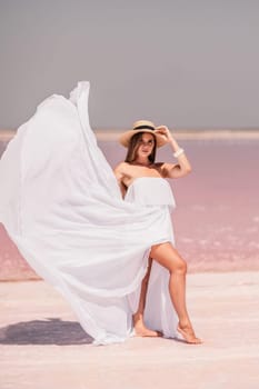 Woman in pink salt lake. She in a white dress and hat enjoys the scenic view of a pink salt lake as she walks along the white, salty shore, creating a lasting memory