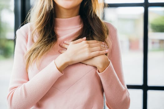 Beauty Asian young woman touching her chest for thanking at home, happy charming female smiling hold hands chest near heart honest with grateful gesture