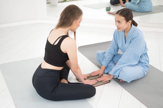 Two women sit on yoga mats with their hands on sadhu boards