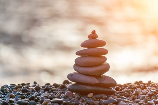 Balanced rock pyramid on pebbles beach. Golden sea bokeh on background. Selective focus, zen stones on sea beach, meditation, spa, harmony, calm, balance concept