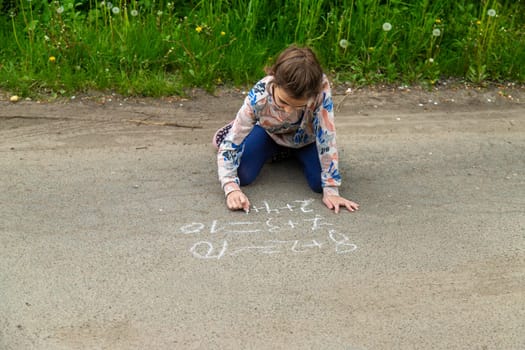 Children draw equations on the pavement with chalk. Selective focus. Kid.