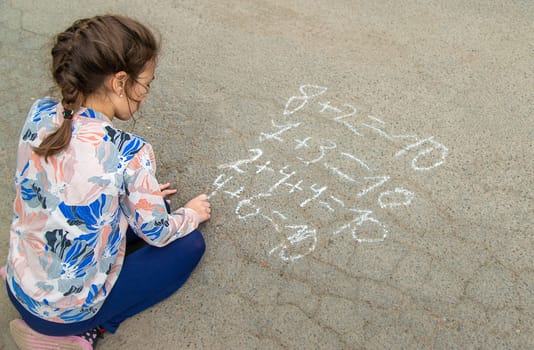 Children draw equations on the pavement with chalk. Selective focus. Kid.