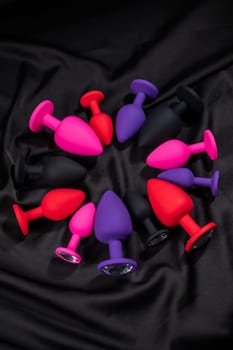 A set of silicone anal plugs in different colors and sizes on a black silk sheet