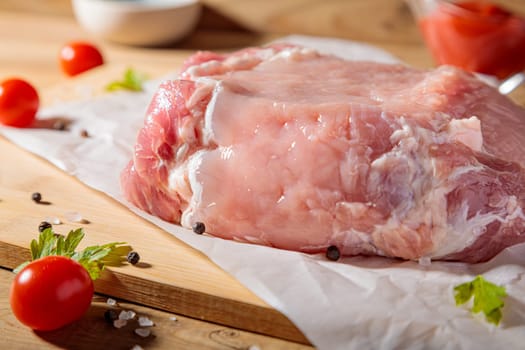 A piece of raw pork meat on a cutting board. Tomatoes, ketchup