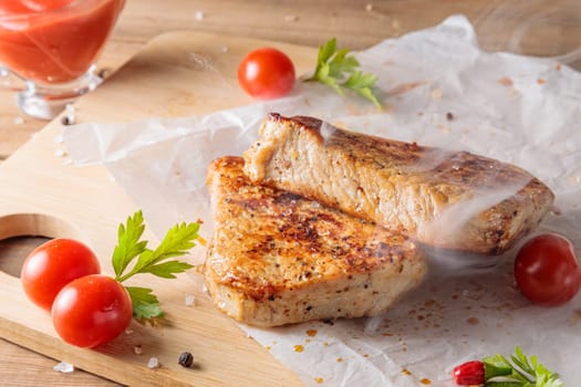 Slices of roast pork meat with tomato and ketchup on a wooden board