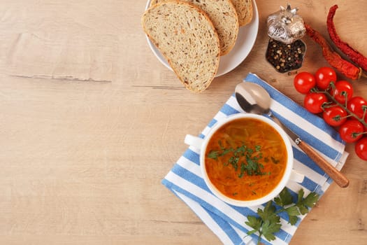 Vegetable soup with potatoes, cabbage, carrots and onions in a white bowl on the kitchen table. Vegetarian food. Copy space