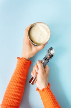 The girl holds in her hands creamy ice cream in a craft bucket. Ice cream spoon. Blue background, copy space