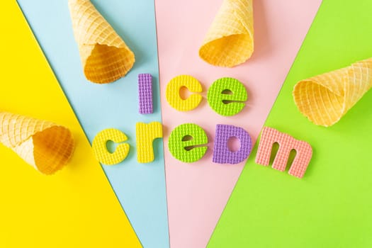 Flat lay composition with a waffle cone and the inscription ice cream on different bright backgrounds. View from above