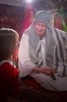 Portrait of young arabian muslim couple in traditional clothes in cozy red room. Fhoto shoot in easten style with male and female model like in harem with a sultan and an odalisque. Partial focus