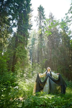 Adult mature woman 40-60 in a green long fairy dress in forest. Photo shoot in style of dryad and queen of nature. Fairy in beautiful green summer forest. Concept of caring for nature