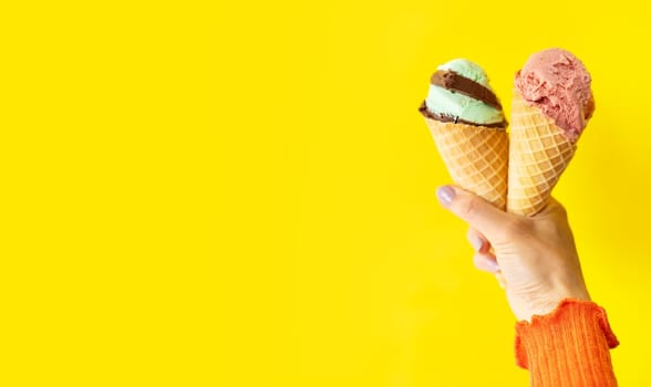 A cone of bright, tasty, refreshing ice cream on a yellow bright background. A woman holds ice cream in her hands, a place for an inscription. The concept of vacation, vacation at sea