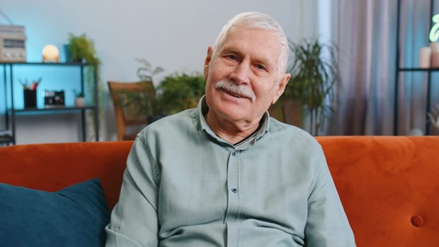 Happy calm senior grandfather man at home couch smiling friendly, glad expression looking away dreaming resting, relaxation feel satisfied concept good news, celebrate win. Elderly guy in living room