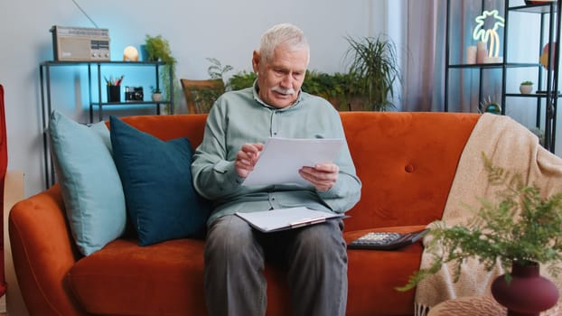Happy senior grandfather man work with documents from home, analyzing information, read business papers prepare financial report at home. Elderly guy winner shocked by sudden victory good success news