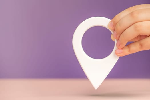 Pin icon or travel nautical map. GPS direction indicator. A hand holds a location sign on a purple background. Laying a route, finding a location. copy space