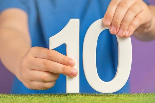 Number 10 in hand. The hand holds a white number ten on a purple background, 10 percent per annum. Advertising banner or greeting card. Concept for World Science Day, November 10th