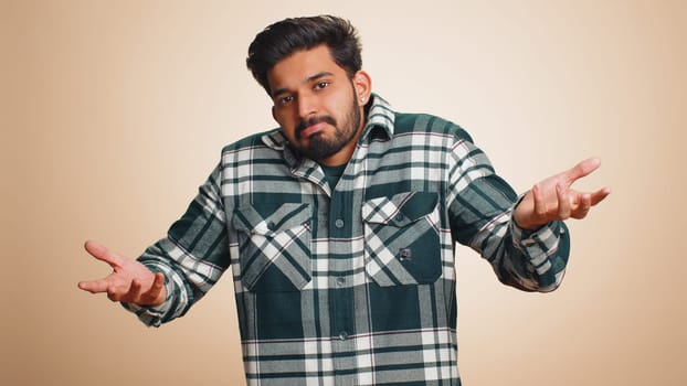 No idea, I dont know answer. Puzzled clueless uncertain indian handsome man raising hands in helpless gesture, embarrassed confused by difficult question. Confused one guy on beige studio background