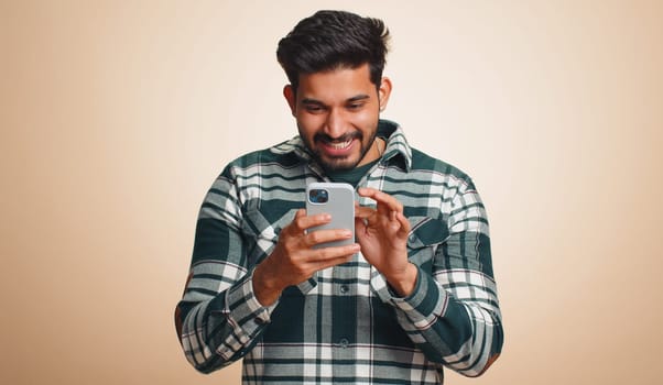 Happy excited joyful indian man in green shirt use smartphone typing browsing shouting say wow yes found out great big win, good news, lottery goal achievemen, celebrating success, winning game