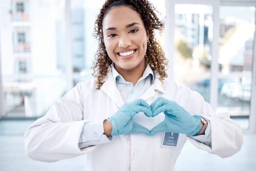 Woman, love and heart hands portrait in hospital for care, trust and support on valentines. Healthcare, dentist and happy black female doctor with hand gesture for affection, romance and kindness