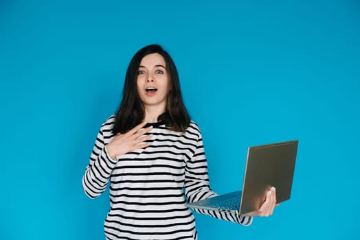 Excited Woman in Striped Sweater Writing Email on Laptop - Modern Technology and Communication Concept. Empty Space for Text - Isolated on Blue Background - Perfect for Business and Technology Themes