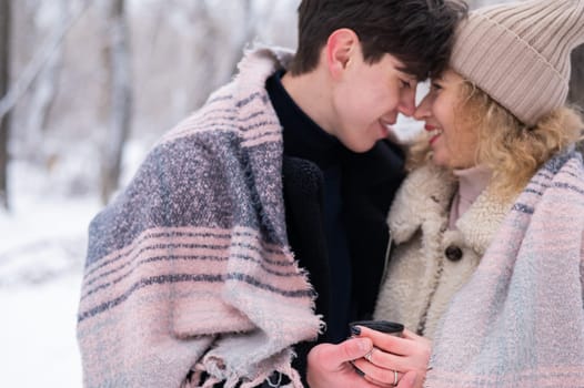 A young couple walks in the park in winter. The guy and the girl are drinking a warming drink outdoors