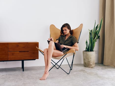 Female student study sits on a chair with a laptop work at home smile and relax, modern stylish interior Scandinavian lifestyle, copy space. High quality photo