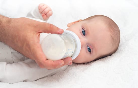 Baby eats formula from a bottle supported by his father.