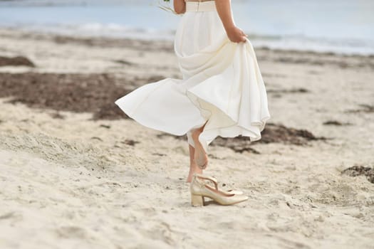 Bride in white dress and golden shoes on the sandy beach